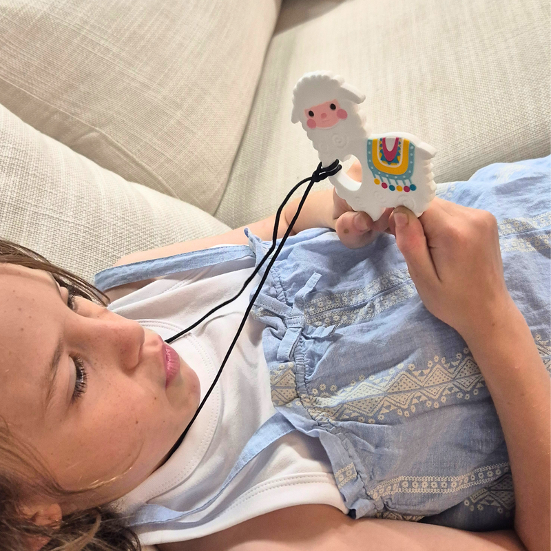 Child wearing a white and yellow llama chewable necklace with the pendant held in hand