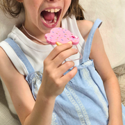Child holding a pink ice cream pendant chew necklace near their mouth while wearing it as a sensory toy