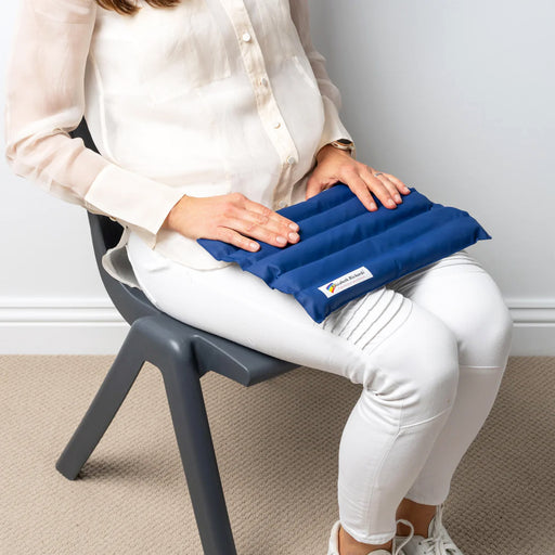 Person sitting on a grey chair holding a blue weighted lap pad on their lap against a plain white wall background.